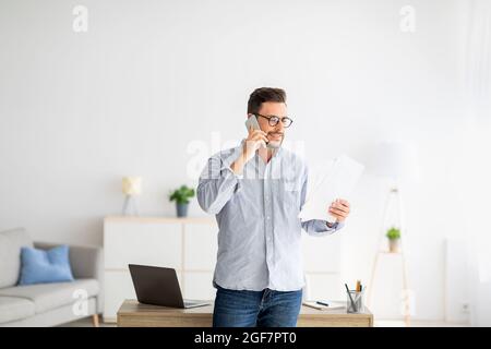 Home Office-Konzept. Selbstbewusster Millennial-Unternehmer, der am Handy spricht und Finanzberichte diskutiert Stockfoto