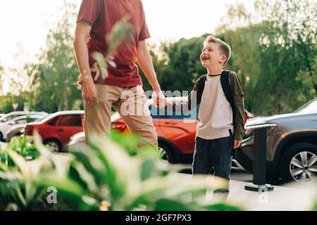 Glücklicher Vater und Kind Sohn gehen in den Unterricht. Eltern nehmen Kind Junge zur Schule in der ersten Klasse. Schüler der Grundschule gehen mit Rucksack im Freien studieren Stockfoto