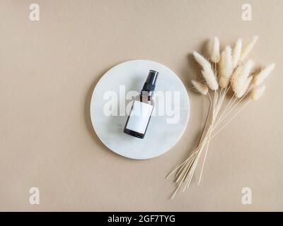 Marmor weißes rundes Podium, bernsteinfarbene Kosmetikflasche mit weißem Label-Mock-Up und Bouquet von trockenem Lagurus auf beigem Hintergrund. Draufsicht. Speicherplatz kopieren Stockfoto