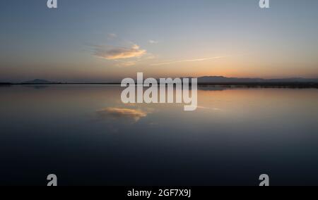 Sonnenuntergang in den Salzebenen von Santa Pola Spanien.am Horizont mit Spiegelung der Wolken auf dem Wasser. Im Hintergrund die Silhouette der Berge. Stockfoto