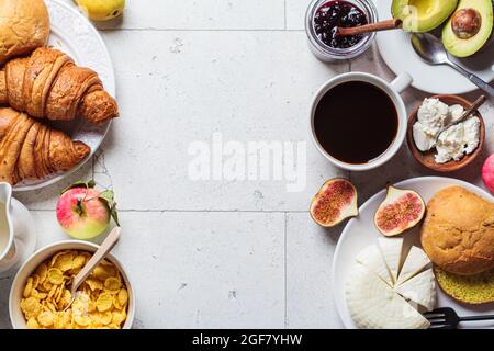Rahmen des Frühstückstisches mit Cornflakes, Croissants, Obst, Käse und einer Tasse Kaffee. Grauer Kachelhintergrund, Draufsicht. Stockfoto
