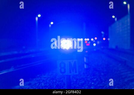 Die blaue Ampel am Nachtbahnhof leuchtet blau. In der Ferne Dunst und leuchtende Laternen. In der Nähe der Eisenbahn.verschwommener Hintergrund. Stockfoto