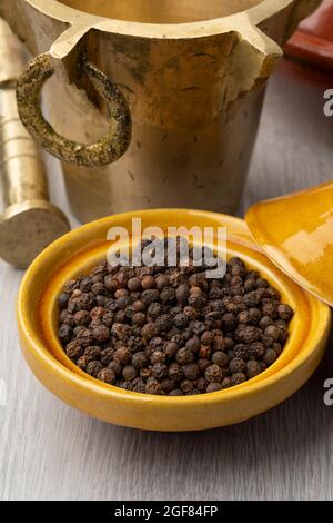 Traditioneller marokkanischer Metallmörtel und Stößel mit einer Tajine getrockneten schwarzen Pfeffersamen in der Front aus nächster Nähe Stockfoto