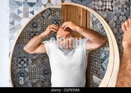 Hübscher, bezaubernder grauhaariger bärtiger Mann vor dem Spiegel im Badezimmer. Männer Hautpflege Morgen Routine. Stockfoto