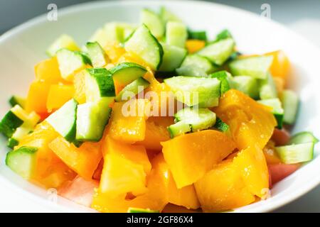 Frische gelbe Tomaten mit Gurke, Gewürzen und Öl auf einem weißen Teller. Konzept der schmackhaften und gesunden Lebensmittel. Sommersalat. Stockfoto