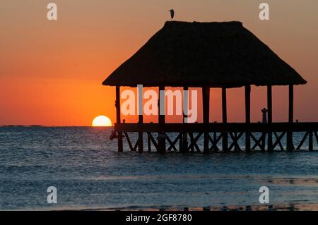 Hölzerner Pier am Meer mit Strohdach bei Sonnenuntergang an einem tropischen Strand auf Holbox Island in Mexiko Stockfoto