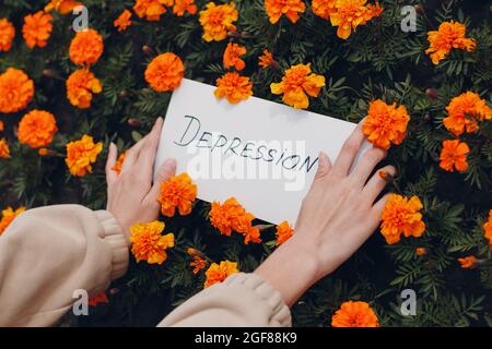 Frau hält in der Hand weißes Blatt Papier mit dem Wort Depression auf Blumenhintergrund. Stockfoto