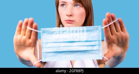 Nahaufnahme einer jungen blonden Frau, die in Pandemiezeit die medizinische Einwegmaske in die Hand hält und aufschaut. Stockfoto