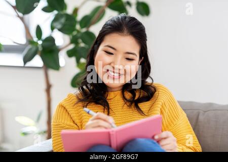 asiatische Frau mit Tagebuch sitzt auf dem Sofa zu Hause Stockfoto