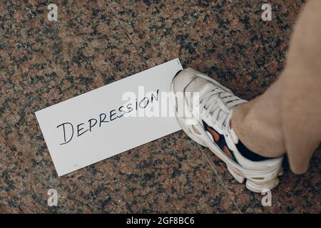 Frau tritt auf weißes Blatt Papier mit dem Wort Depression und Fuß darauf. Stockfoto