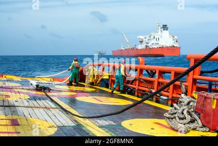 Zwei erfahrene Schiffsbesatzungen, die den Frachtschlauch von FPSO an den Erdöltanker in der Mitte auf See anschließen Stockfoto