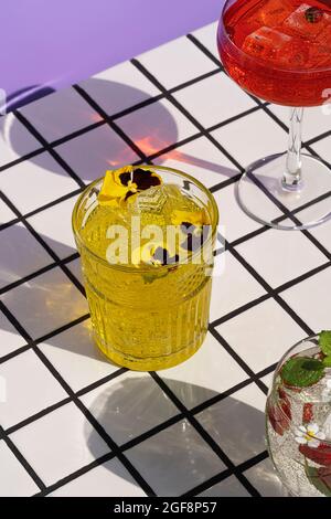 Bunte Cocktails mit Sonnenschatten stehen auf den Fliesen und purpurem Hintergrund. Blick von oben. Stockfoto