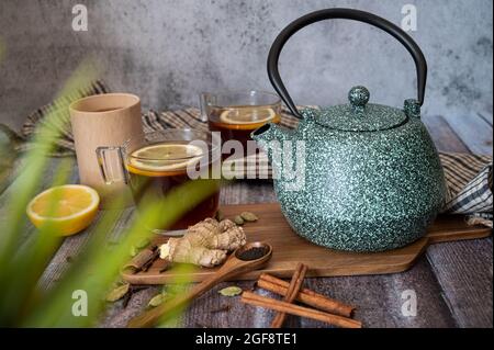 Gesunder Tee in durchsichtige Tasse gegossen. Teekannen, Zitrone, Ingwer, Kardamom, Heidekraut und Glasglas mit Gänseblümchen-Heilkräutern. Stockfoto