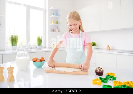 Foto von fröhlich glücklich kleines Mädchen halten Nudelholz machen Teig Kuchen Hobby drinnen Hausküche Stockfoto