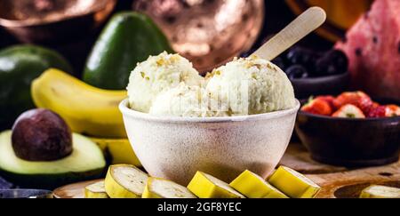 Hausgemachtes und veganes Bananeneis ohne Milch in einer recycelten Kunststoffschüssel, mit Früchten im Hintergrund Stockfoto