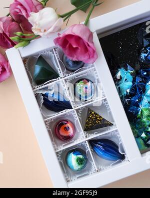 Geschenkschachtel mit handgefertigten Pralinen. Geometrisches und Raumdesign. Box auf einem hellen Hintergrund. Süßigkeiten und Süßigkeiten aus nächster Nähe. Vertikales Foto Stockfoto