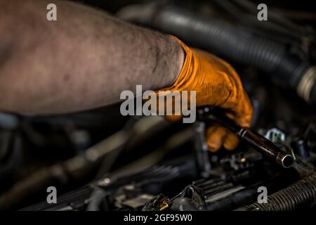 Ein Mann mit orangefarbenen Handschuhen, der in einer Autowerkstatt einen Motor repariert und repariert Stockfoto