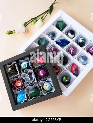 Geschenkschachtel mit handgefertigten Pralinen. Geometrisches und Raumdesign. Box auf einem hellen Hintergrund. Süßigkeiten und Süßigkeiten aus nächster Nähe. Vertikales Foto Stockfoto
