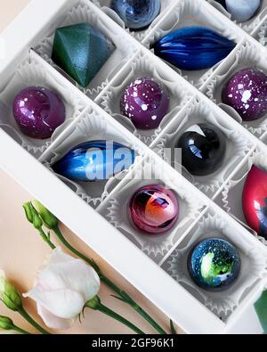 Geschenkschachtel mit handgefertigten Pralinen. Geometrisches und Raumdesign. Box auf einem hellen Hintergrund. Süßigkeiten und Süßigkeiten aus nächster Nähe. Vertikales Foto Stockfoto