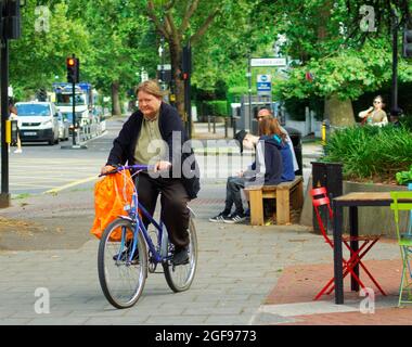 London, Großbritannien. August 2021. Alter Flugzeugbaum bedroht durch temporäre Radweg. Radfahrer und ein Polizeiauto kommen an einem Flugzeugbaum vorbei, der angeblich mindestens 90 Jahre alt ist und gefällt werden soll, um Platz für eine temporäre Fahrradspur auf der Chiswick High Road, London, zu schaffen. Die derzeit umstrittene temporäre Fahrbahn wird nicht von allen genutzt. Kredit: Peter Hogan/Alamy Live Nachrichten Stockfoto