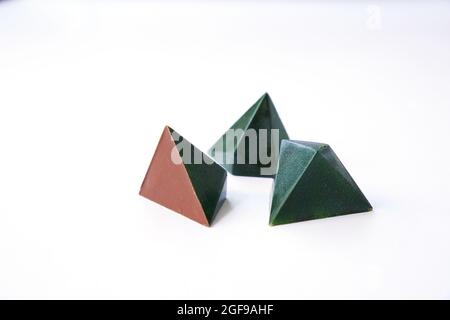 Luxuriöse pyramidenförmige Schokoladenbonbons. Drei Pralinen - grüne Farbe und geometrisches dreieckiges Bonbon-Design. Handarbeit. Isolierte Süßigkeiten auf Weiß Stockfoto