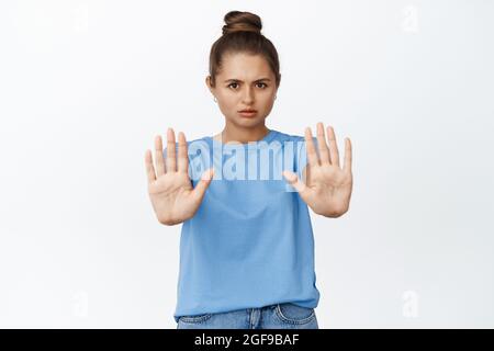 Die junge Frau, die gestikuliert hat, hört auf, nein zu sagen, streckt die Hände aus, um etwas Schlimmes zu verbieten, und steht auf weißem Hintergrund Stockfoto