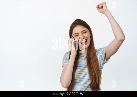 Glückliches Mädchen im Gespräch auf dem Handy und feiern. Aufgeregt Frau erhalten gute Nachrichten auf Abruf, stehen vor weißem Hintergrund Stockfoto