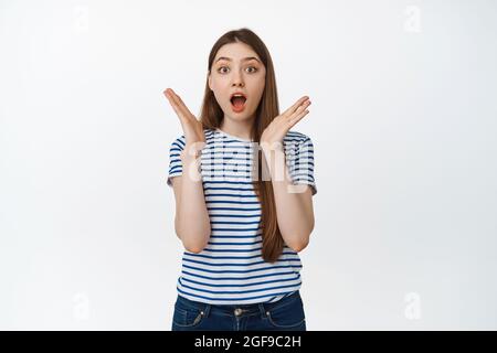 Portrait of surprised girl starren erstaunt auf Kamera, keuchend und sagen wow beeindruckt, stehend über weißem Hintergrund Stockfoto