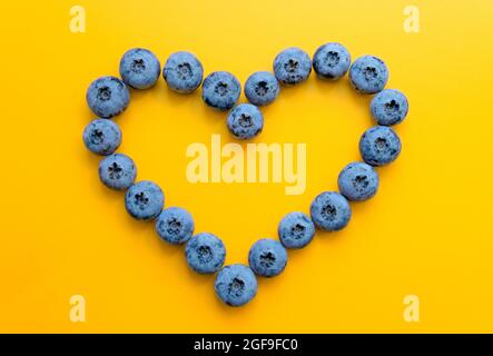 Herzsymbol aus Heidelbeeren auf gelbem Hintergrund. Herzgesundheitskonzept. Stockfoto