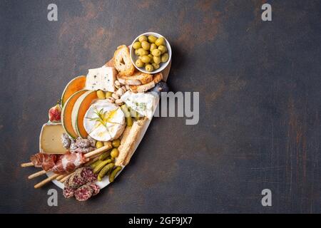 Verschiedene Käsesorten auf Holzbrettteller, Oliven, Trauben, Brot auf schwarzem Stein-Hintergrund, Draufsicht, flaches Lay, Kopierraum. Stockfoto