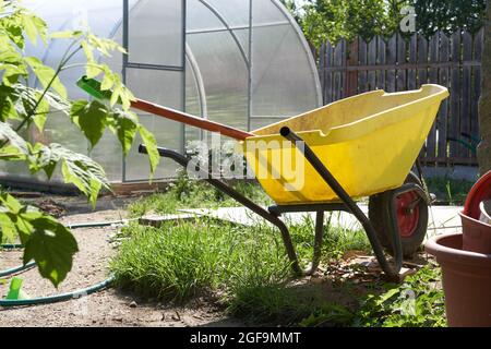 Nahaufnahme eines modernen Polycarbonat-Gewächshauses. Landwirtschaftliche Werkzeuge und ein Wagen mit einem Rad im Garten. Das Konzept des modernen Gartenbaus. Hochwertige Fotos Stockfoto