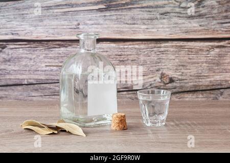 Auf einem Holztisch befindet sich eine ungekorkte Flasche Schnaps mit einem leeren Etikett und einem vollen Schnapsglas. Der Stopfen der Flasche ist neben ihr und es gibt al Stockfoto