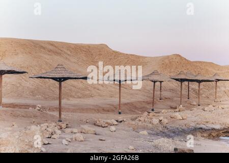 Sandige und felsige Küste mit Palmen-Sonnenschirmen in Paspelfarben. Desolate Resort beidge Strand an der Küste des Roten Meeres. Sharm el Sheikh, Sinai Stockfoto