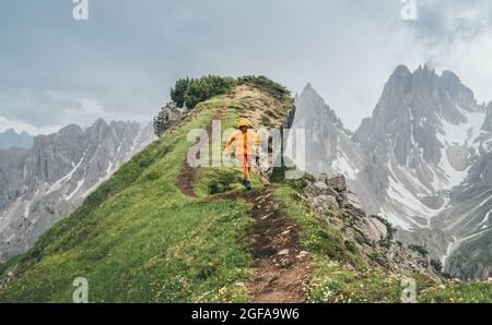 Gekleidet leuchtend orange Softshell Jacke Läufer läuft durch grüne Bergweg mit malerischen Dolomiten-Alpen-Bereich Hintergrund,. Aktive Menschen und Europ Stockfoto