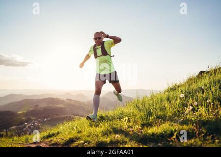 Active Mountain Trail Läufer gekleidet hellen T-Shirt mit einem Rucksack in Sport Sonnenbrille laufen Ausdauer Ultramarathon Rennen durch malerische Hügel an Stockfoto