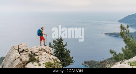 Junger Wanderer Backpacker Mann mit Trekkingstöcken genießen das Mittelmeer auf Clifftop während Lycian Way Trekking Walk. Berühmte Likya Yolu Türkisch Stockfoto