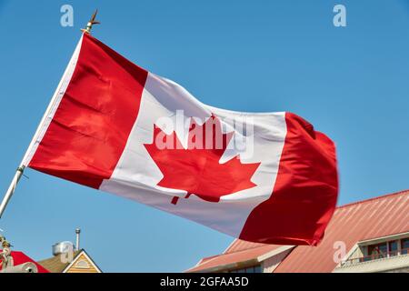 Blauer Himmel Mit Kanadischer Flagge. Eine kanadische Flagge, die an einem sonnigen Tag in einer steifen Brise flattern wird. Kanada. Stockfoto