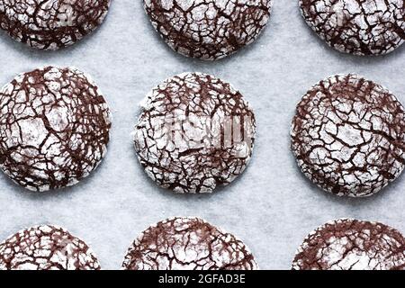 Hausgemachte Schokolade crinkle Cookies in Pulverzucker auf einem Pergamentpapier. Hintergrund der Speisen. High-Angle-Ansicht. Stockfoto