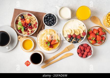 Ein Tisch für ein gesundes Frühstück mit Pfannkuchen, Müsli, frischen Beeren, Kaffee mit Milch und Orangensaft. Draufsicht. Stockfoto