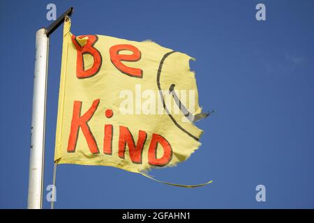 East Wittering, Großbritannien, 23. August 2021: Eine zerfetzte gelbe Flagge mit der Botschaft "sei freundlich" und die Reste eines Smiley-Gesichts fliegen vor den Hintergrund o Stockfoto