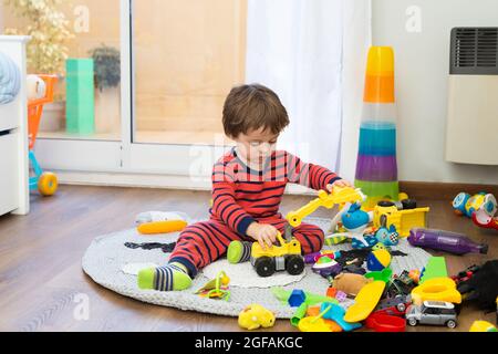 Kleines Kleinkind spielt einsam mit vielen Spielsachen in seinem Schlafzimmer. Stockfoto