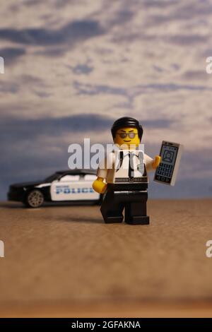 GREENVILLE, USA - 31. Jul 2021: Eine vertikale Aufnahme einer Figur des Lego-Polizisten, die ein Mobiltelefon vor einem Polizeiauto hält Stockfoto