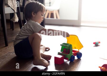 Einsames Kleinkind, das mit seinen Spielsachen im Wohnzimmer auf dem Boden spielt. Stockfoto