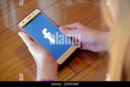 Mädchen mit Handy in den Händen und einem Facebook-Logo auf dem Bildschirm. Junge Frau, tausendjährig. Technologie. Soziales Netzwerk. Stockfoto