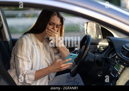 Weinendes junges Mädchen las Nachricht auf dem Handy. Frustriert verärgert junge Frau am Fahrersitz im Auto Stockfoto