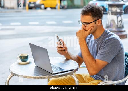Der junge latein betonte, draußen mit Handy und Computer zu arbeiten. Stockfoto