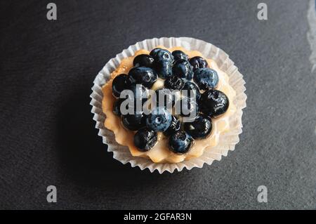 Tarte mit Heidelbeeren ist auf einem schwarzen Hintergrund aus Naturstein. Stillleben mit süßen Kuchen mit wilden Beeren auf dunklem Grund Stockfoto