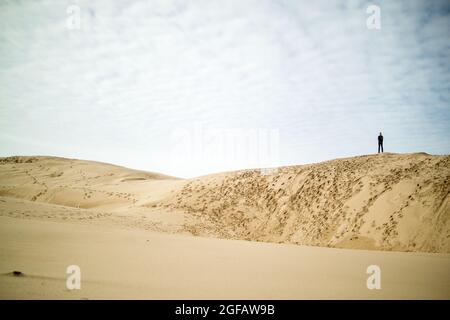 Eine Einzelfigur (Mann), die am Wintertag auf großen Sanddünen steht Stockfoto