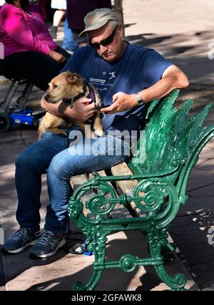 Ein Mann entspannt sich mit seinem Hund auf einer Bank in einem öffentlichen Park in Santa Fe, New Mexico. Stockfoto