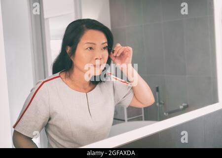 Asiatische reife Frau Putting Mascara suchen in LED-Lichtrahmen Spiegel Anwendung Make-up immer bereit für die Arbeit zu Hause Badezimmer. Chinesische ältere Dame Stockfoto